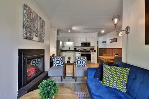 Living space with comfortable seating, an electric fireplace, and a fully-equipped stainless kitchen.