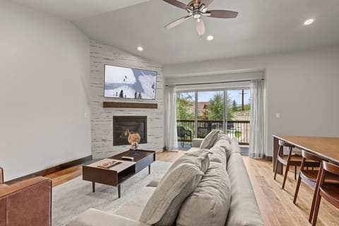 Unwind in your bright, modern living room featuring a cozy fireplace, large TV, and plush seating. Through your private balcony doors, you'll enjoy scenic views framed by natural light.