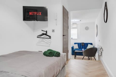 A bright double bedroom that opens onto the living area, featuring a wall-mounted Smart TV, clothes hanger, and private ensuite.
