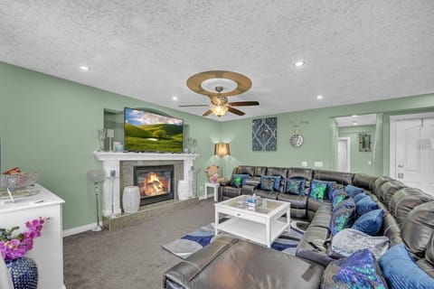 Large leather sectional with reclining chairs await for a relaxing family time together in the family room with a large smart TV, IPTV box, cable, boardgames, mini library, snacks table, and fireplace.