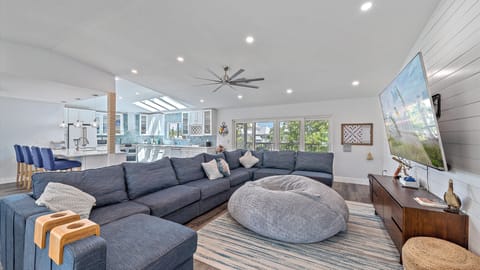 Unwind in the open and inviting living room, featuring a massive sectional sofa, shiplap accent wall, and a large Smart TV, all bathed in soothing coastal decor for ultimate family comfort.