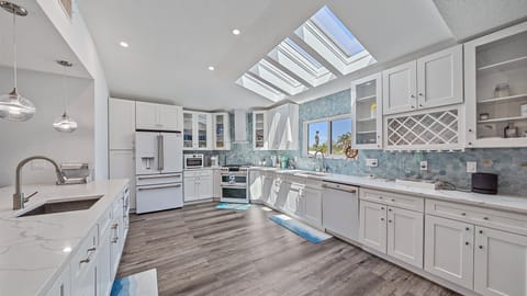 The spacious gourmet kitchen is a chef’s delight, featuring sleek white cabinetry, a striking blue coastal-themed backsplash, and an abundance of natural light for preparing delicious meals during your Sarasota stay.