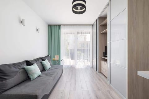Modern living room with a large window, green curtains, grey sofa, and light wooden flooring.