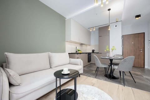 A cozy living room space with a soft gray sofa and a dining table for two. Warm lighting and neutral decor create a relaxing atmosphere.