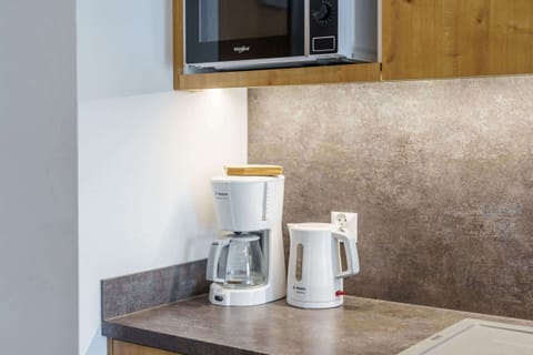 A kitchenette featuring a microwave and wooden cupboards, styled in a clean, minimalistic design.