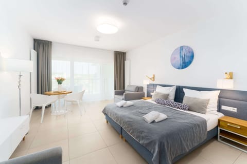 A spacious living room with a double bed, two side tables, and a large window with a modern painting on the wall.