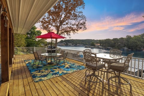 Lakeside deck with stunning sunset views, cozy seating, vibrant decor, and a BBQ grill—perfect for relaxing or dining.