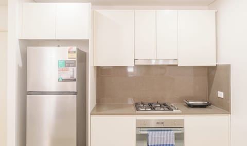 A compact kitchen area featuring sleek white cabinetry, a large stainless steel refrigerator, and a modern built-in oven.