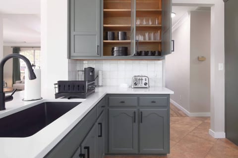 This kitchen boasts a modernized color palette, equipped with a kitchen sink and complete utensils neatly stored in the cupboards. Additional cabinets provide ample space for organizing other kitchen essentials, ensuring a seamless cooking experience