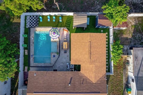 Aerial view showcasing the heated pool, life-size chess, bean bags, fire pit under a gazebo, outdoor dining, BBQ grill, pool loungers, and volleyball and basketball games—all designed for endless outdoor enjoyment.