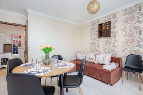 A cozy living room with a round dining table set for four. The space is decorated with floral wallpaper and warm wood tones, creating a traditional and homey atmosphere.