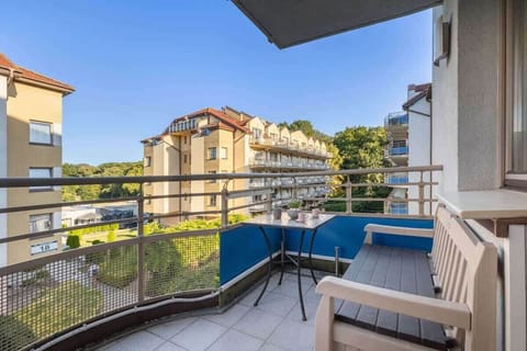 A second view of the balcony with seating and a view of surrounding apartment buildings. The balcony railing is sturdy, and there are a few plants that add a touch of greenery.