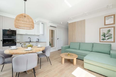A bright and modern living room with a mint green sectional sofa, a wooden coffee table, and a dining area in the background featuring a round table with elegant chairs.