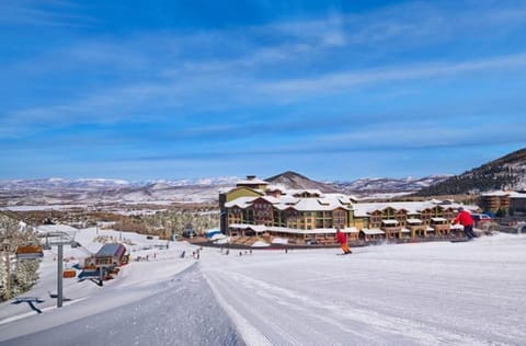 As skiers carve their way down the freshly groomed slopes, the Grand Summit Hotel looms beautifully in the background, framed by a breathtaking winter landscape under a brilliant blue sky.