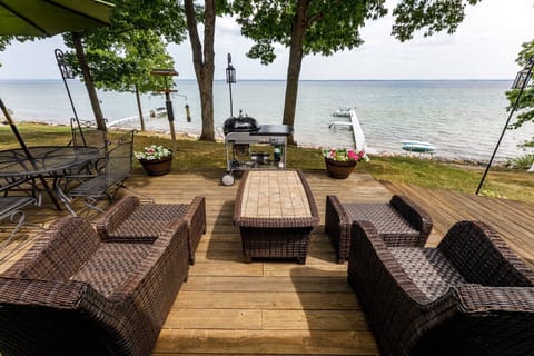 Spacious lakeside deck w/ woven seating, grill & dining table, all set beneath shady trees overlooking the water.