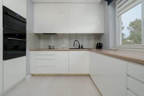White modern kitchen with light flooring and black sink.