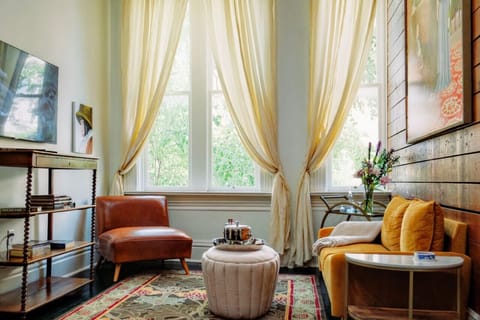 Light filled living room overlooking Main Street with original artwork, original shiplap, flat screen streaming tv, books, silk curtains.