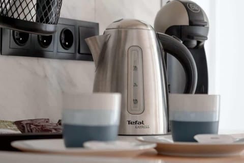 Close-up of a wooden countertop with an electric kettle, mugs, and coffee-making accessories.