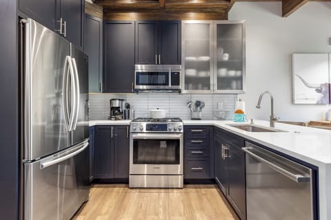 Modern kitchen with stainless steel appliances, dark cabinets, white countertops, and light wood flooring.