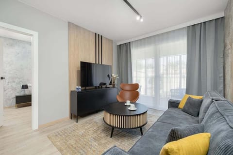 A bright living room with a gray sofa, coffee table, armchair, and large window with sheer curtains.
