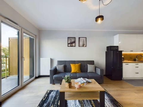  A bright living room with large glass doors opening to a balcony, featuring modern furniture and wooden flooring.