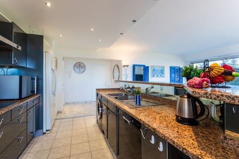 Kitchen connected to the living room with black cabinets, granite countertop, extractor fan, stainless steel sink, and modern appliances.