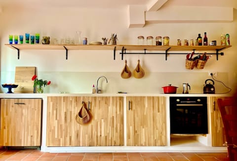 The fully equipped kitchen offers modern appliances, wooden shelves, and ample storage. Light wood cabinets and tiled floors create a bright, airy feel, with an open-plan layout that connects seamlessly to the living and dining areas, ideal for socializin