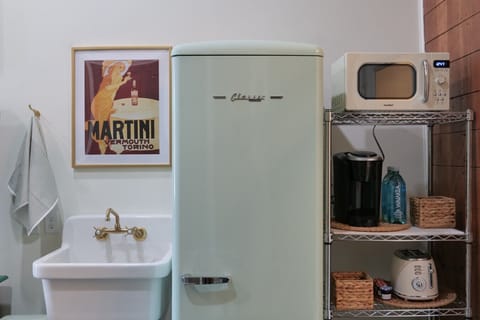 China sink with brass fitting, retro style refrigeration, microwave, toaster, and Keurig with coffee pods.