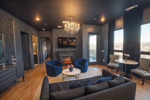 Enjoy a modern, open-plan living space with vibrant blue furniture, a sofa bed, and a stylish kitchen with stainless steel appliances and pendant lighting. A chandelier adds elegance to the cohesive design.