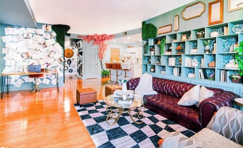 Whimsical Uptown Charlotte condo featuring statement bookshelves, checkerboard rug, and leather sofa. Open layout with office nook, free parking, Sky Lounge and pool access—perfect for stylish mid-term stays near dining and stadiums.