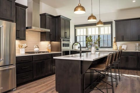 - Cook, gather, and sip in a chef’s kitchen filled with sunlight and sleek style
- Dark cabinets, brass pendants, and a wide island set the scene for memorable meals
- From breakfast spreads to wine nights, this space does it all
