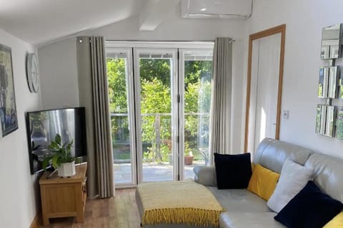 Room with bifold doors to the patio. L shaped sofa, TV with apps. There is an air conditioner for cooling or heating depending on the time of year.
