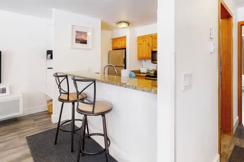 A kitchen area with a granite countertop, two high chairs, wooden cabinets, stainless steel appliances, and a framed picture on the wall.