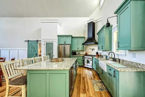 Stylish kitchen featuring a large granite island, farmhouse sink, and modern green cabinets, ideal for culinary enthusiasts