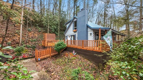Stylish woodland retreat featuring a wraparound deck, flower-filled landscaping, and forest views.