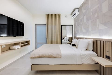 A modern bedroom with a sleek TV mounted on the wall, a large mirror, and a comfortable bed with plush pillows.
