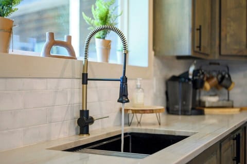 Modern farmhouse kitchen faucet with spring pull-down sprayer and potted plants on a quartz counter.
