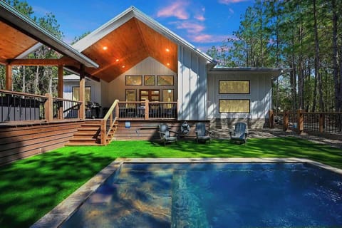 Private backyard oasis with swimming pool, synthetic turf, and spacious wood deck in forest setting.
