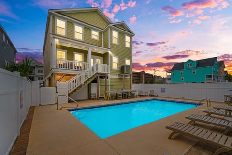 A beautiful two-story beach house with private pool illuminated against a stunning sunset sky in a colorful coastal neighborhood.
