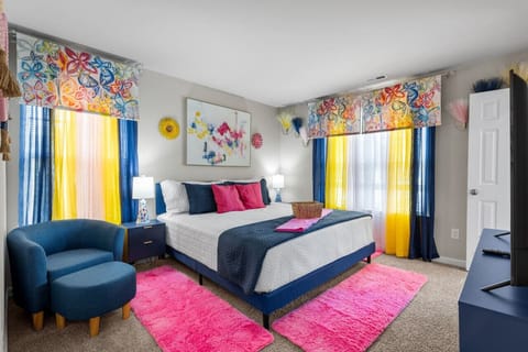 Bright and colorful bedroom with a king-sized bed, a flat-screen Roku TV, and a walk-in closet transformed into a home office. Work remotely in comfort with an ergonomic chair and desk bathed in natural light from the window.