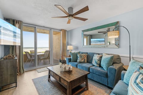 This inviting living room features plush seating, coastal décor, and a rustic coffee table. Sliding glass doors lead to a private patio with ocean views, providing a seamless indoor-outdoor living experience perfect for relaxation.