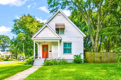 A white home with red accents, nestled in greenery, offers a suburban retreat