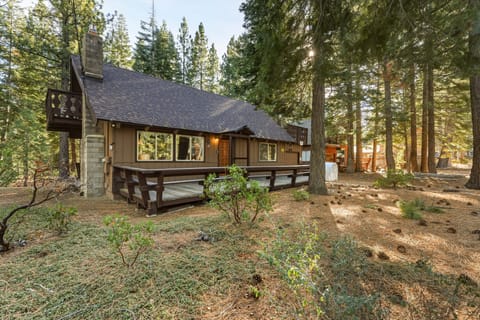 House exterior with front railing, upper railing, chimney, yard, and tall pines around the home.