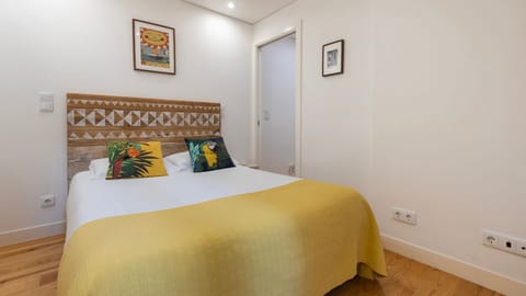 A cheerful bedroom with colorful pillows, wooden textures, and a warm yellow blanket for a relaxing stay. #RestfulRetreat #TropicalVibes