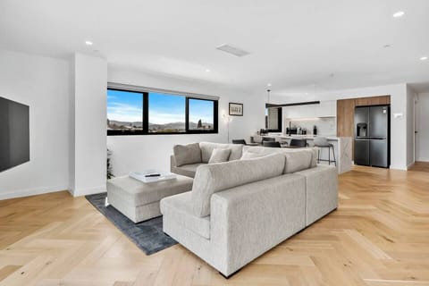 Relax in the open-plan living area featuring a plush L-shaped lounge and mounted TV, with easy access to the private balcony through glass sliding doors.