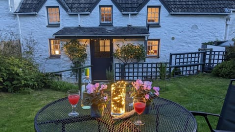 Garden at night with outdoor fairy lights on outdoor table and around cottage entrance