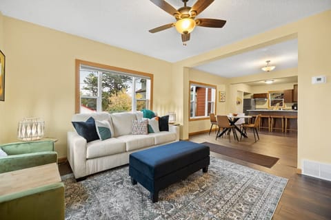 The living room features a comfortable sofa, seamlessly connected to an open-plan space with an island and chairs, alongside tables that offer a perfect blend of relaxation and dining areas.