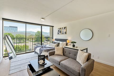 Bright living area w/ cozy sofa & large windows opening to a balcony w/ city views