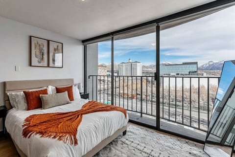 🛏️ Cozy bedroom with plush bedding, warm accents, and sweeping city-to-mountain views from the private balcony 🌆🏔️