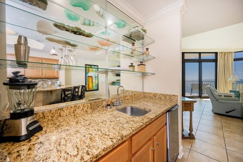Wet bar area with granite countertops, blender, ice-maker, and a view of the cozy living area and balcony beyond
